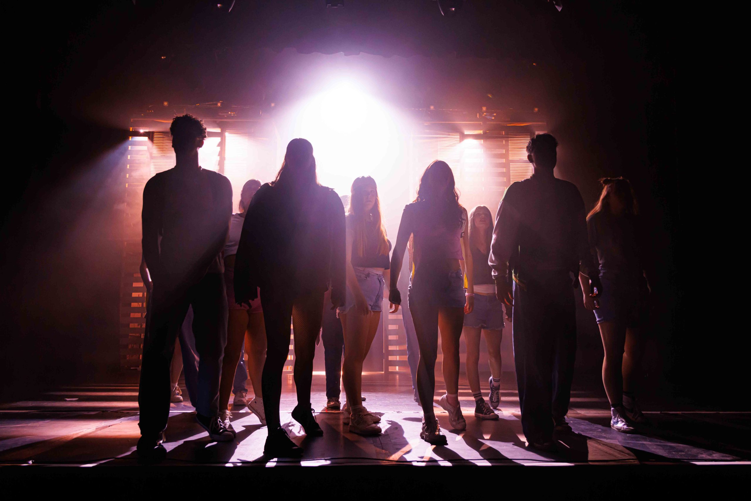 Students walk upstage in silhouette towards a wall of bright warm light.
