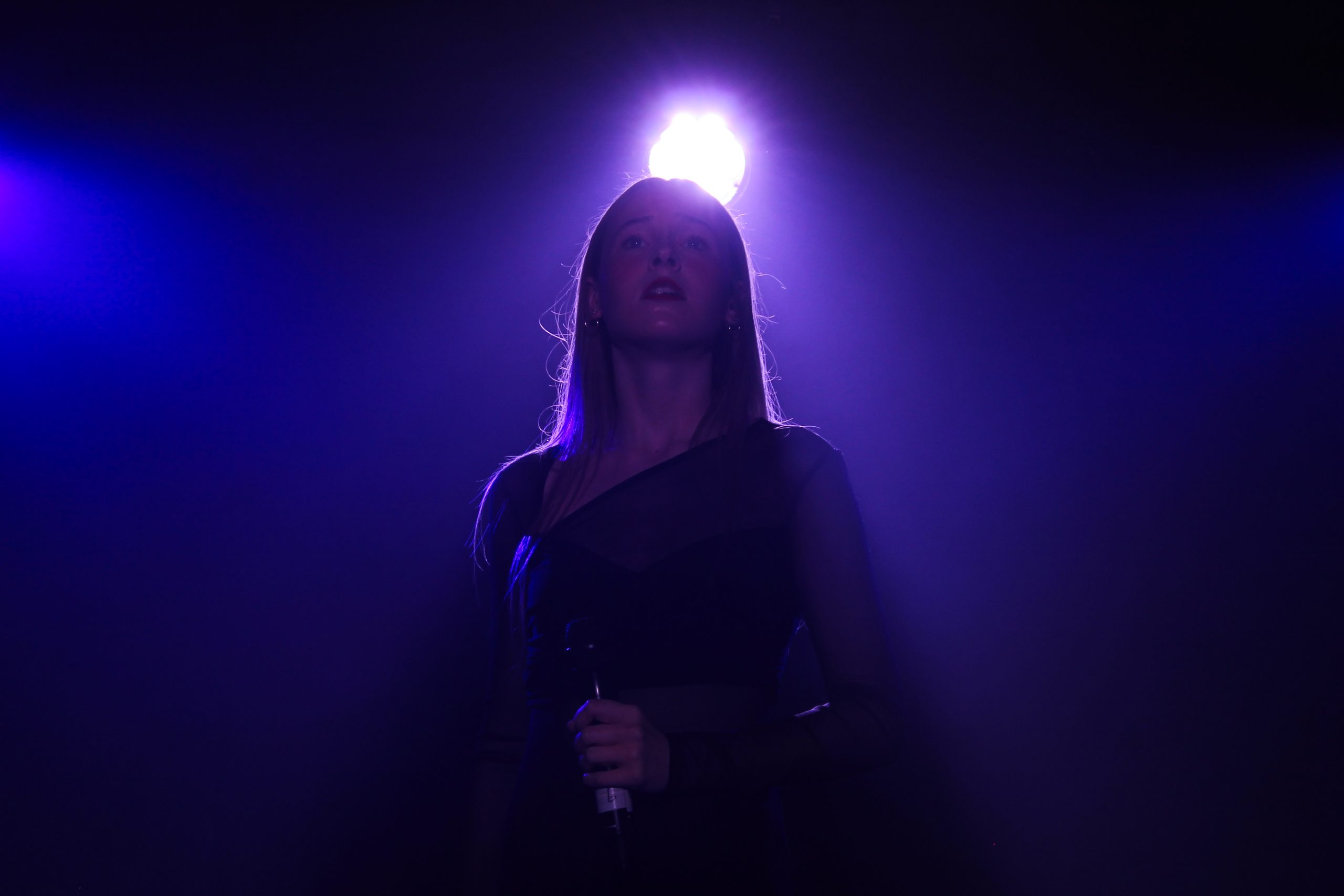 A singer in a black dress is backlit by a purple spotlight.