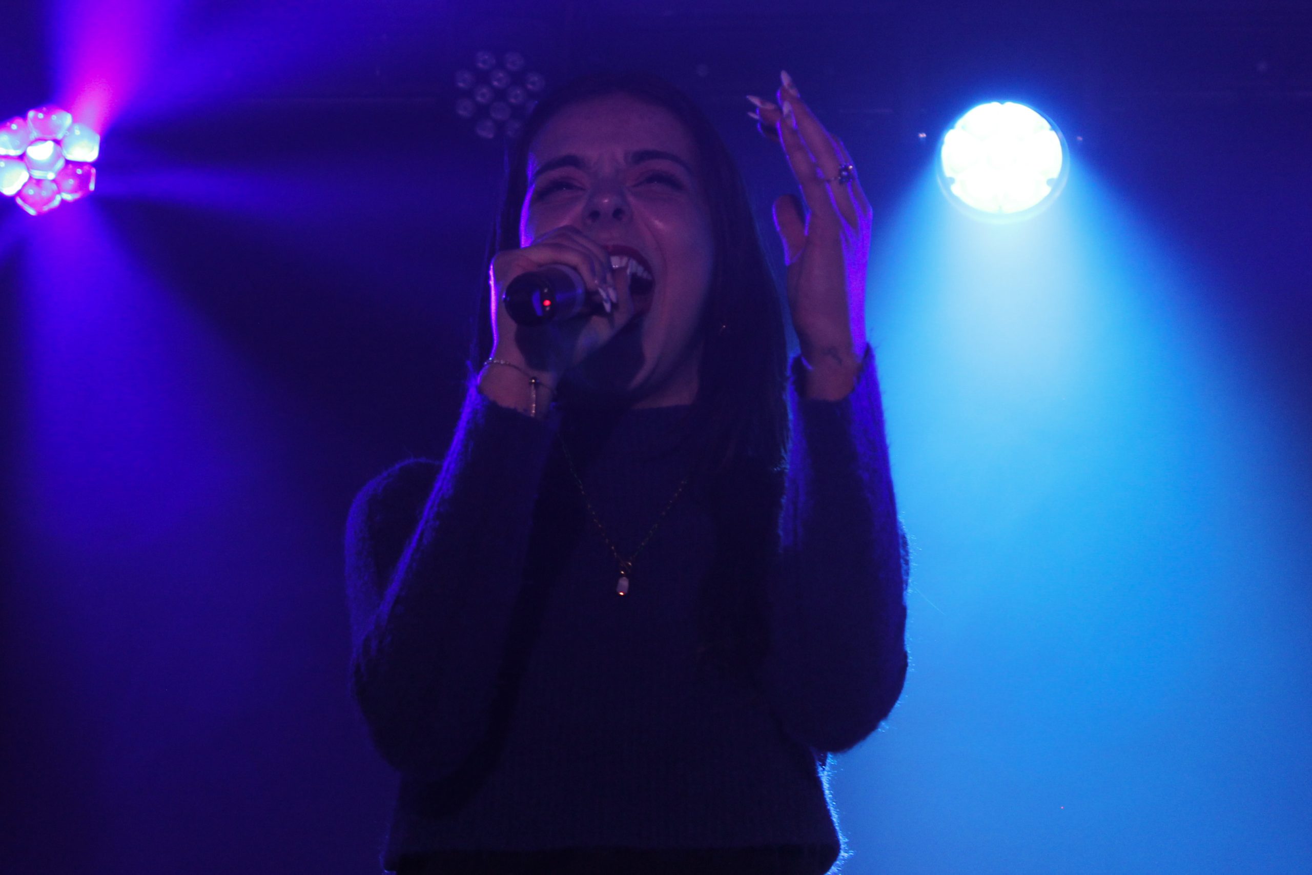 A young woman sings with her eyes closed under blue and purple lights.