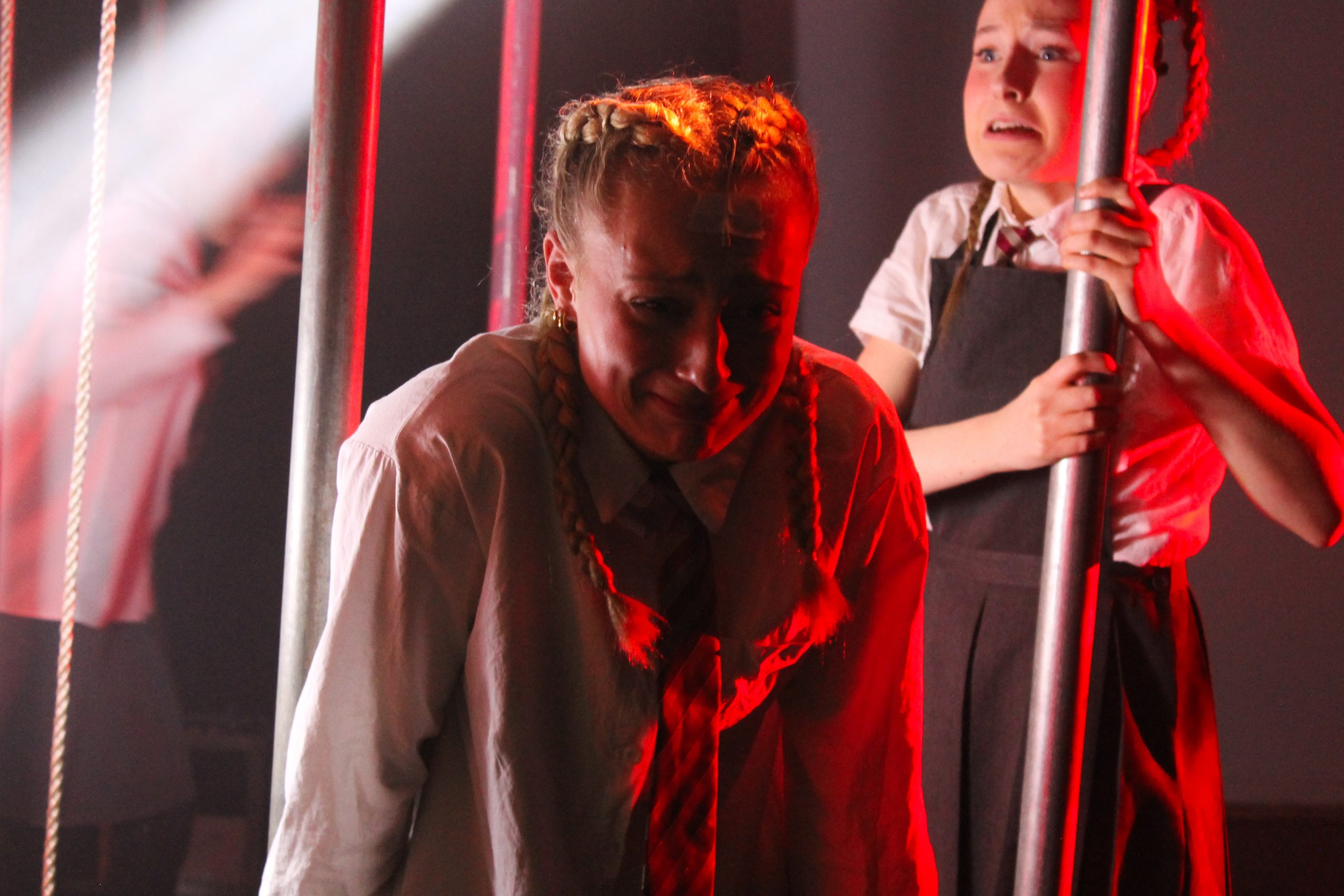 Two pupils in school uniform, one with plaited hair, cling to poles in red light.