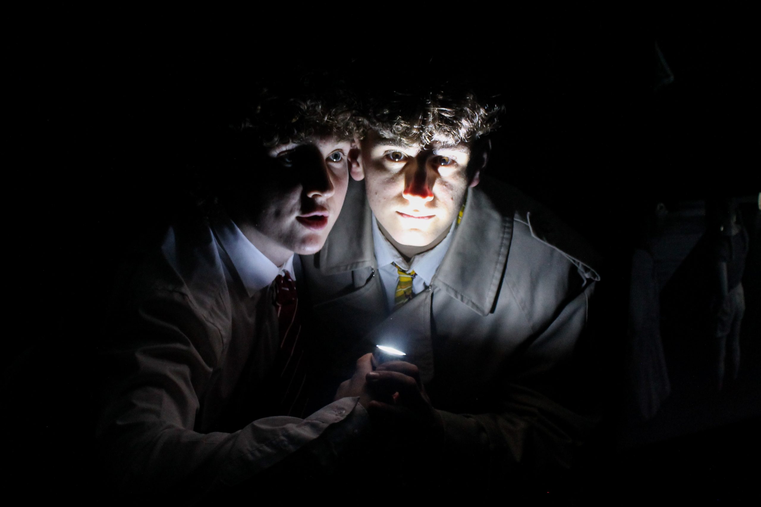 Two pupils huddle in the dark, their faces lit by a torch.