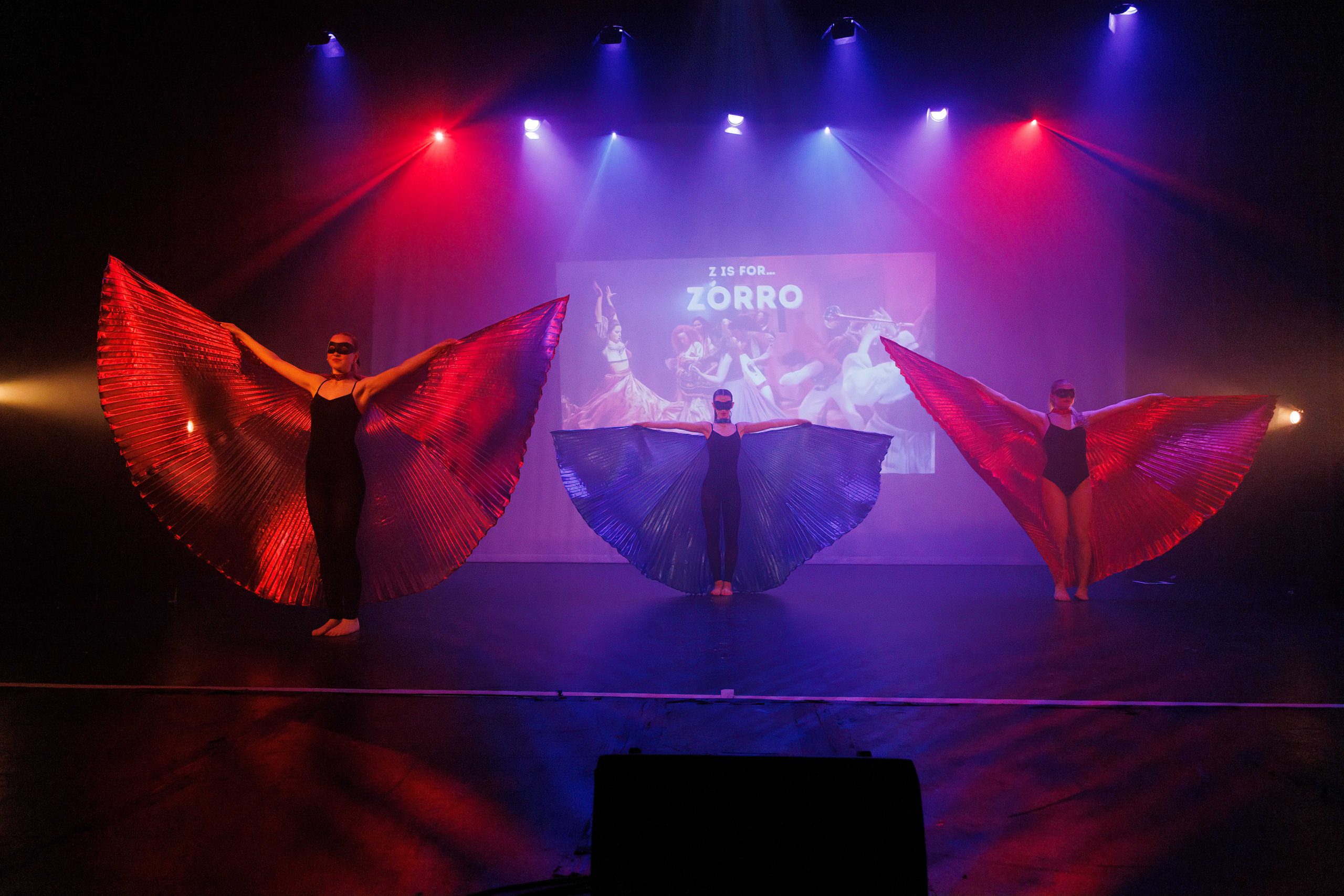 Dancers spread large red and blue fan wings in front of a screen reading 'Z is for Zorro'.