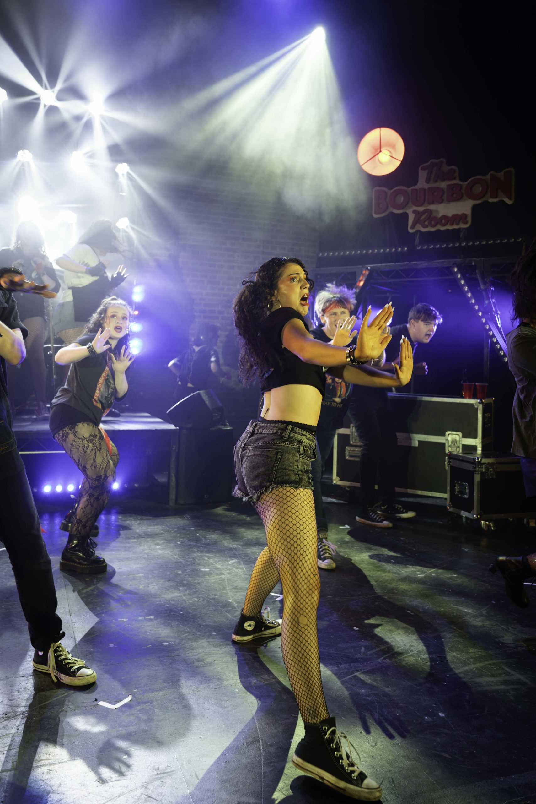 A dancer in denim shorts and fishnets performs in front of 'The Bourbon Room' sign.