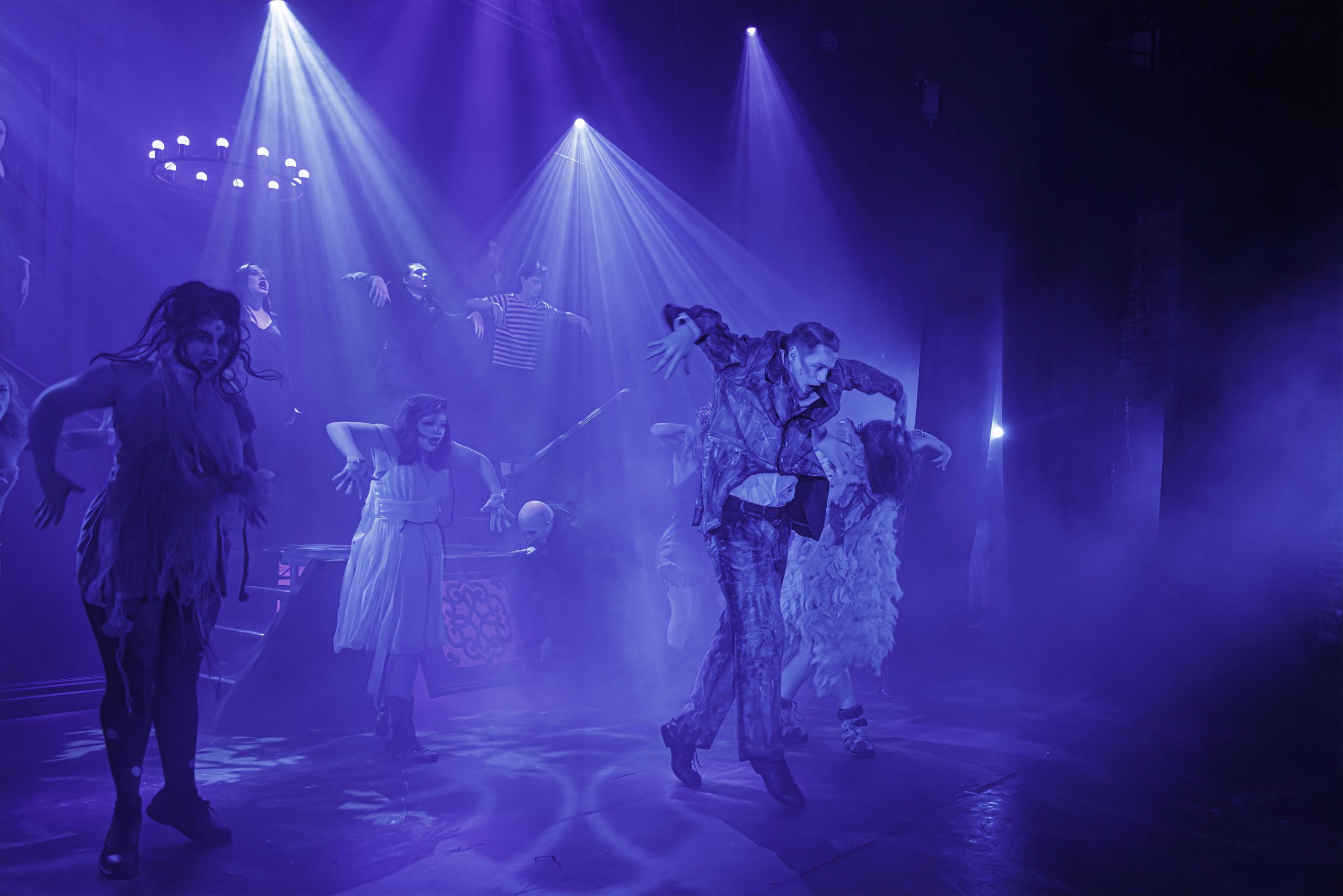 Ancestors in ragged grey costumes strike angular dance poses in a haze of blue and purple light.